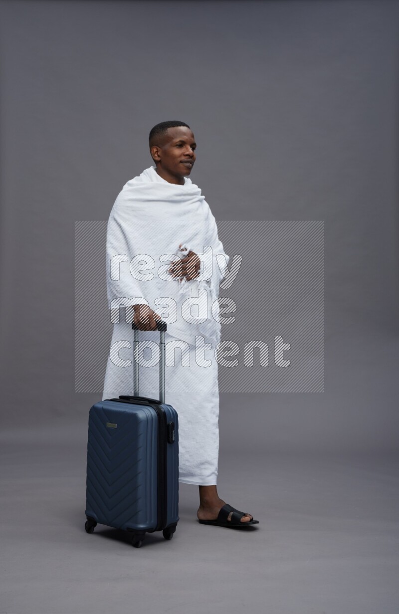 A man wearing Ehram Standing holding traveling bag on gray background