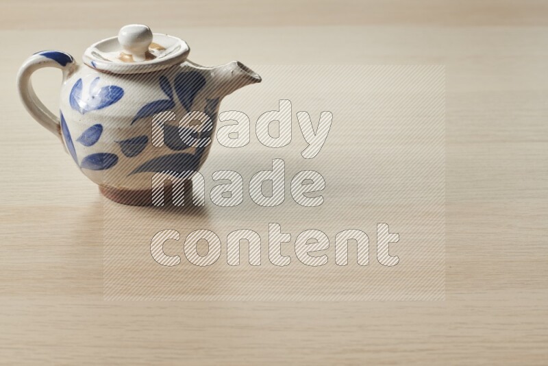 A pottery teapot on light wooden background