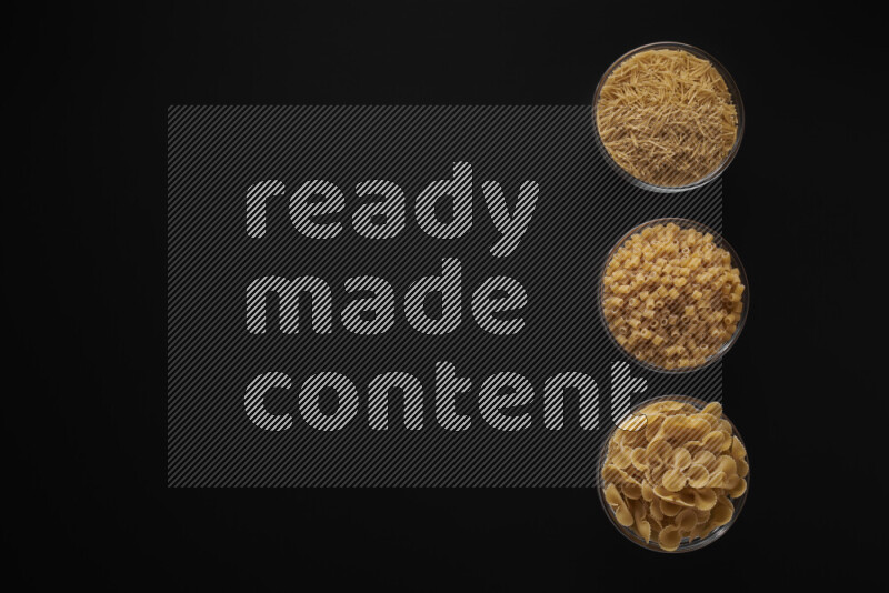 Different pasta types in 3 glass bowls on black background