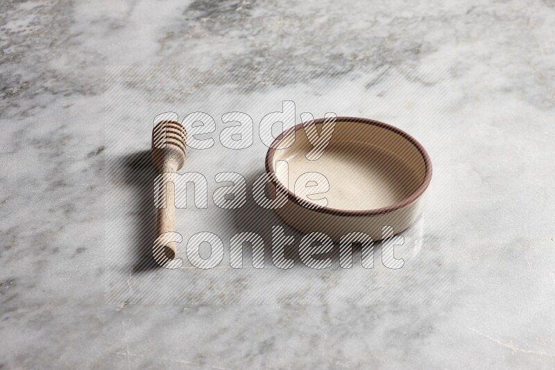 Beige pottery oven bowl with wooden honey dipper on the side on grey marble background
