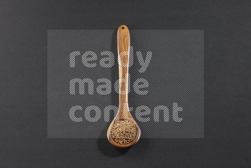 ملعقة خشبية كبيرة ممتلئة ببذور الخردل علي خلفية سوداء