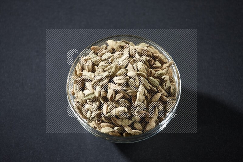 A glass bowl full of cardamom on black flooring