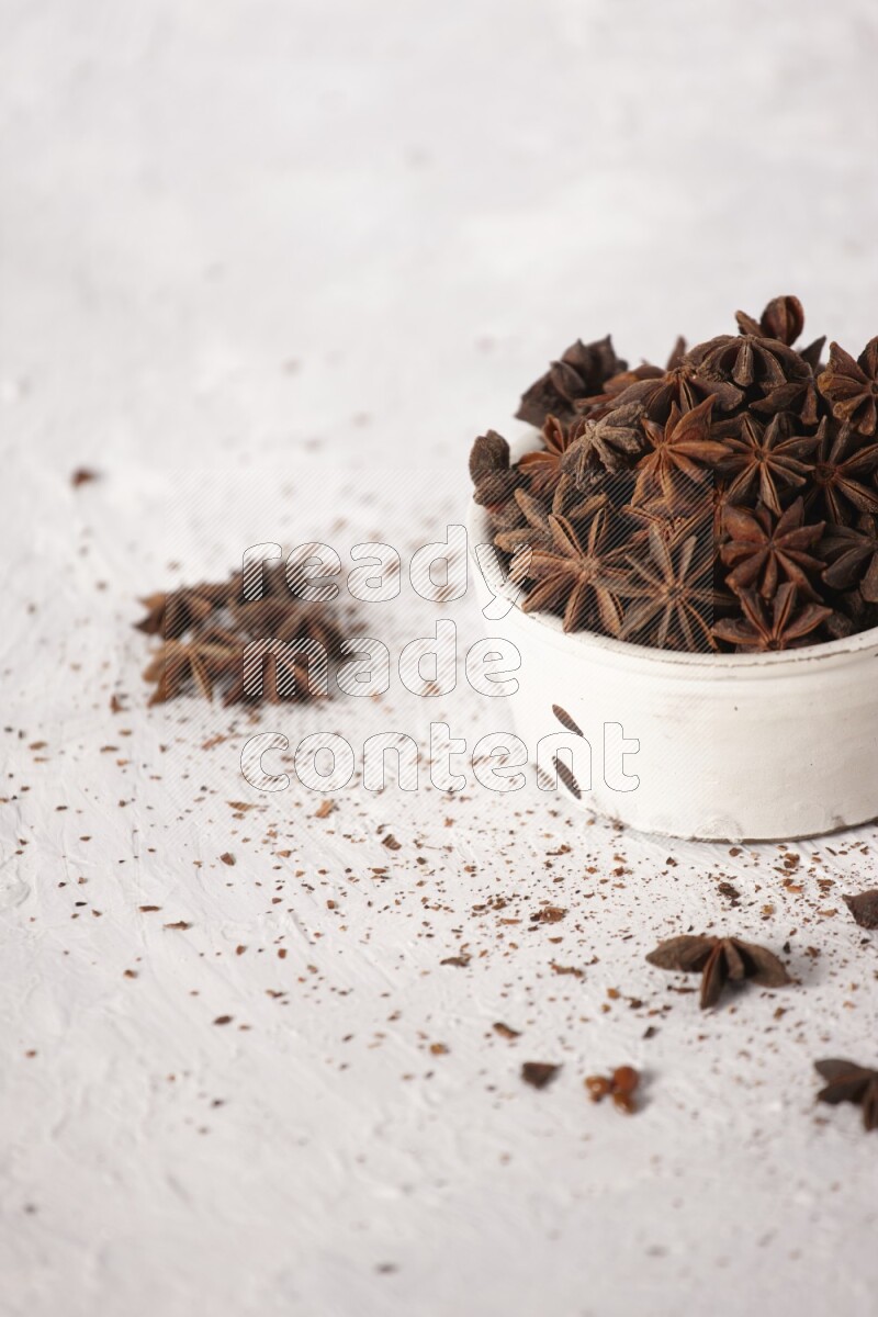 Star Anise in a white bowl and more of it sprinkled on white background
