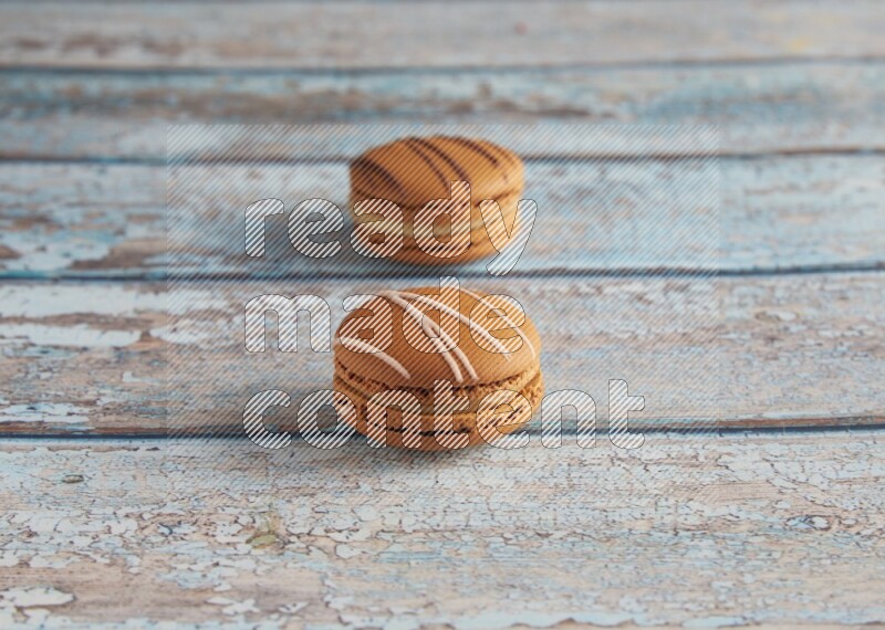 45º Shot of of two assorted Brown Irish Cream, and light brown Almond Cream macarons next to each other on light blue background