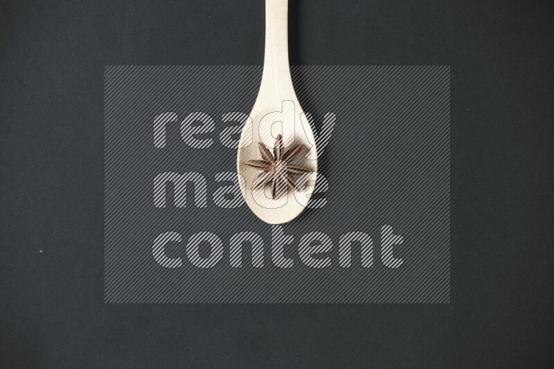Star Anise in a wooden spoon on more stars anise filling the frame on black flooring