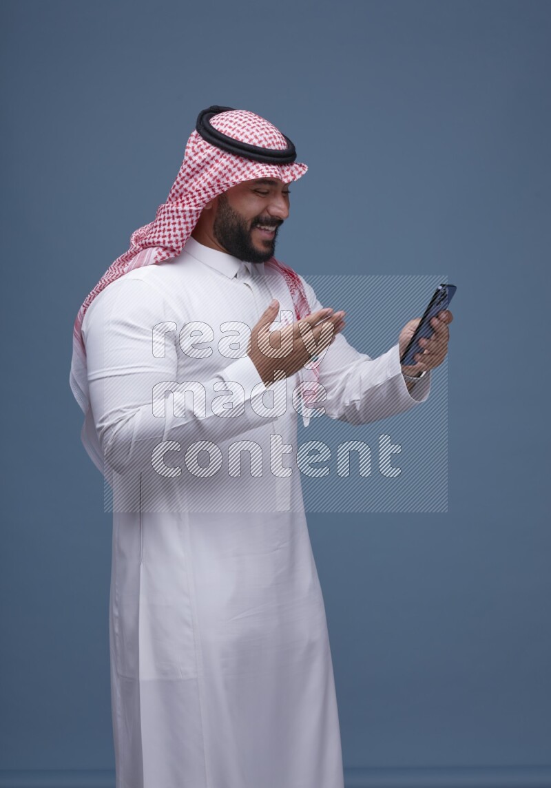 A man Texting on Blue Background wearing Saudi Thob and Shomag