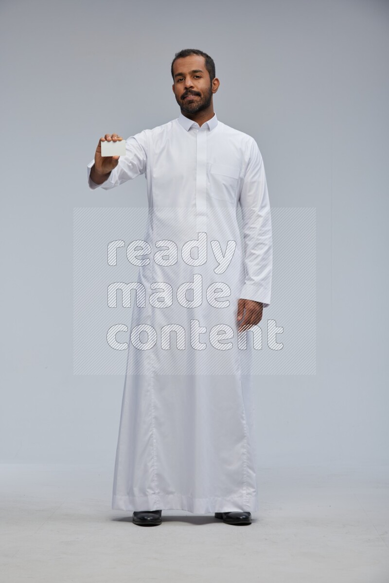 Saudi man wearing Thob standing holding ATM card on Gray background