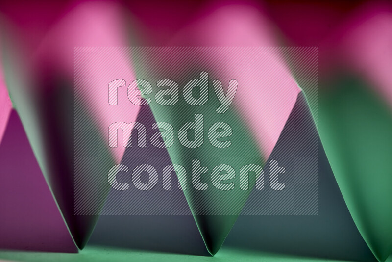 A close-up abstract image showing sharp geometric paper folds in green and pink gradients