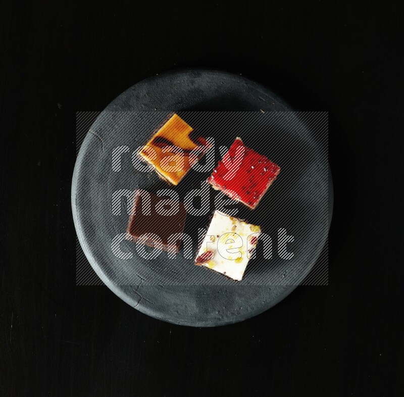 Assorted desserts in a black pottery plate on black background