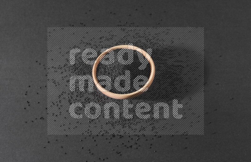 وعاء خشبي ممتلئ ببذور حبة البركة محاط ببعض البذور علي خلفية سوداء