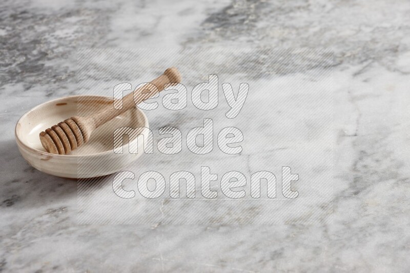 Beige pottery bowl with wooden honey dipper in it on grey marble background