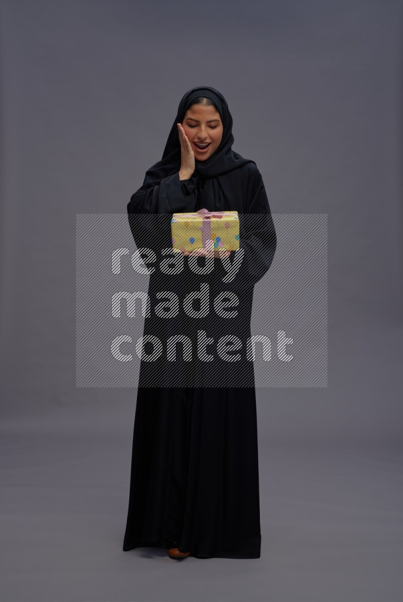Saudi woman wearing Abaya standing holding gift box on gray background