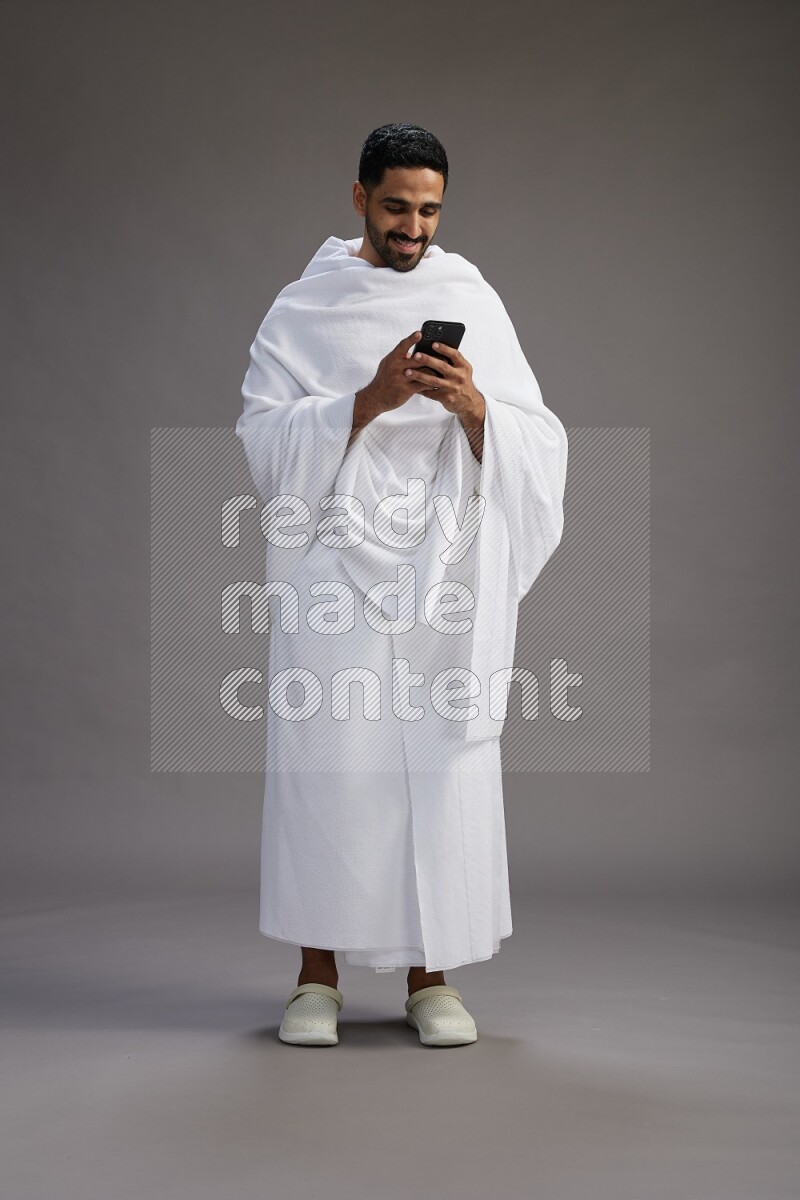 A man wearing Ehram Standing texting on phone on gray background