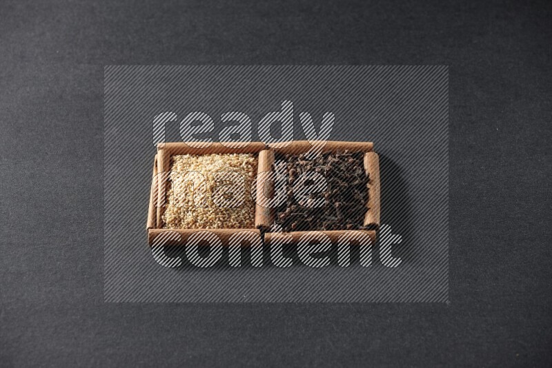 مربعان من أعواد القرفة ممتلئان ببذور السمسم والقرنفل علي خلفية سوداء