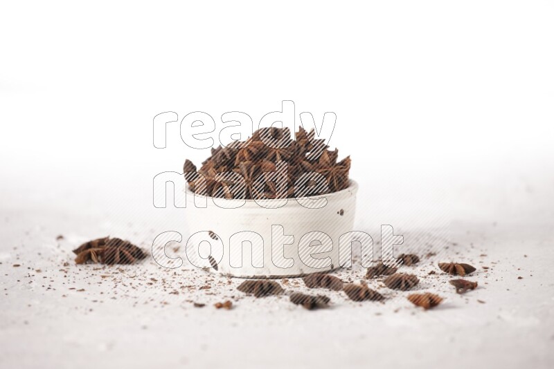 Star Anise in a white bowl and more of it sprinkled on white background
