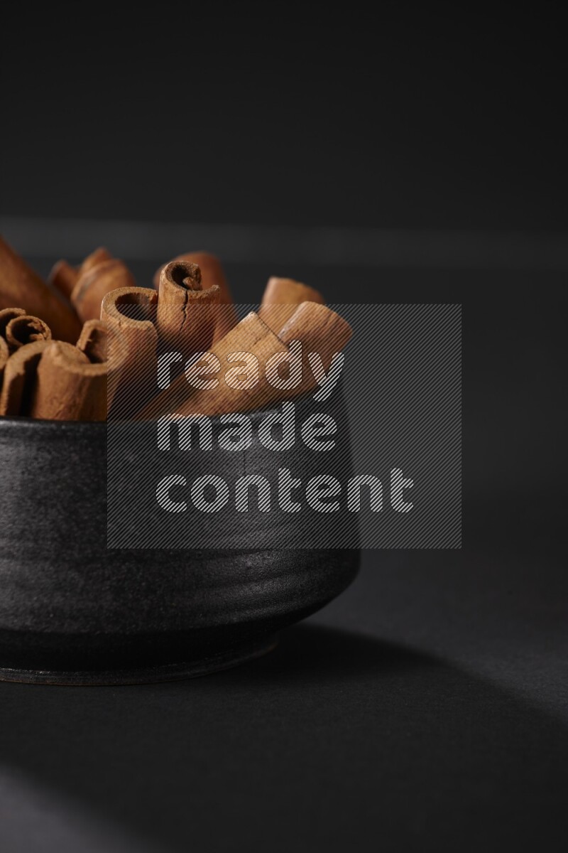 Cinnamon sticks in a black bowl on a black background in different angles