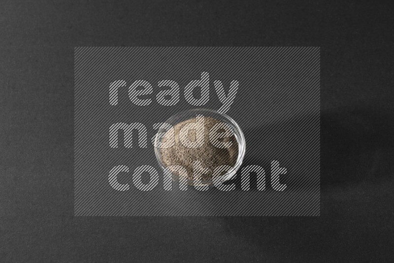 A glass bowl full of black pepper powder on black flooring