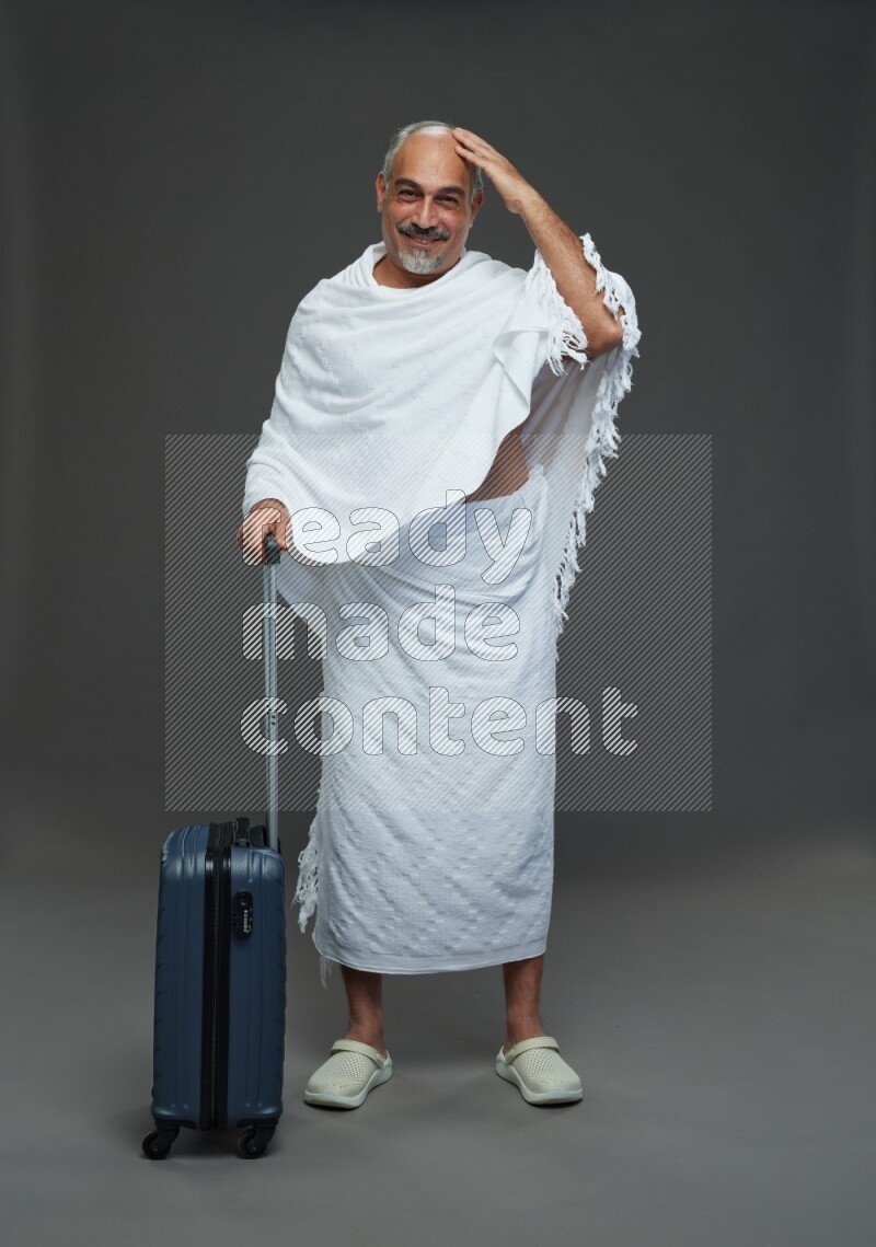 A man wearing Ehram Standing holding traveling bag on gray background