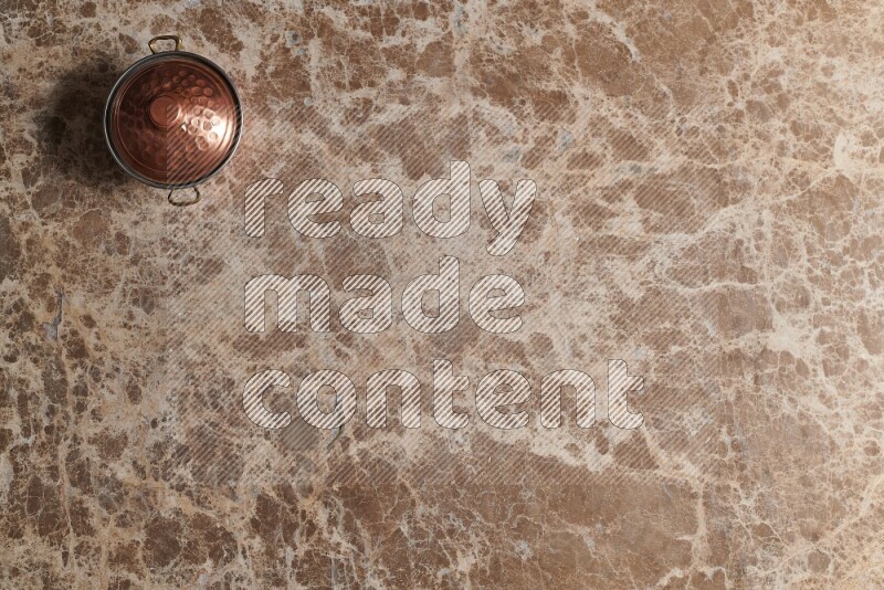 A small copper pot on beige marble background