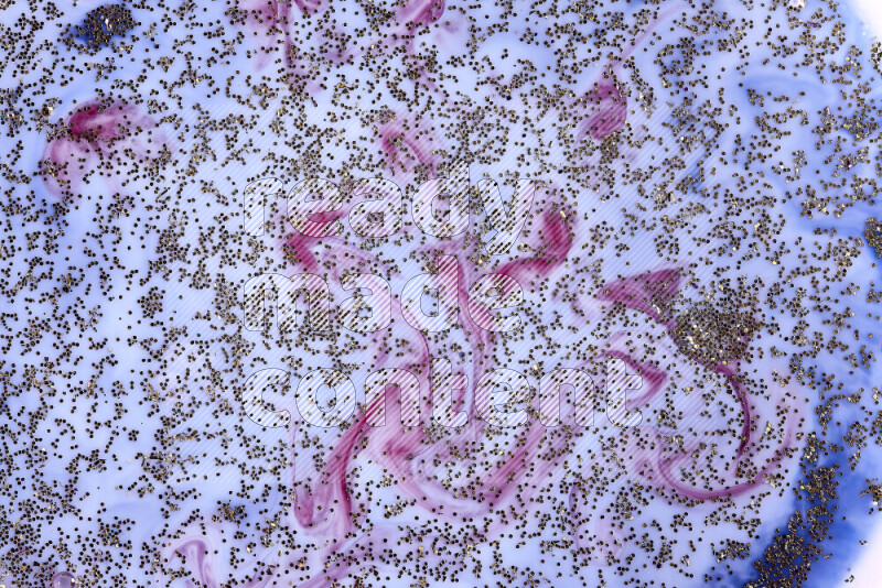 A close-up of sparkling gold glitter scattered on swirling blue and red background