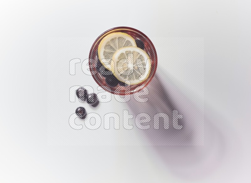 Blue transparent glass filled with blueberries decorated with lemon slices on a white background