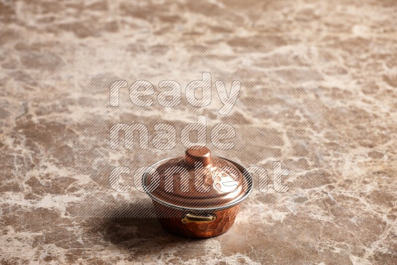 A small copper pot on beige marble background