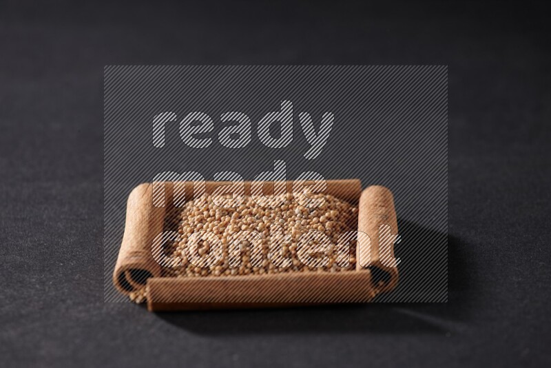 A single square of cinnamon sticks full of mustard seeds on black flooring