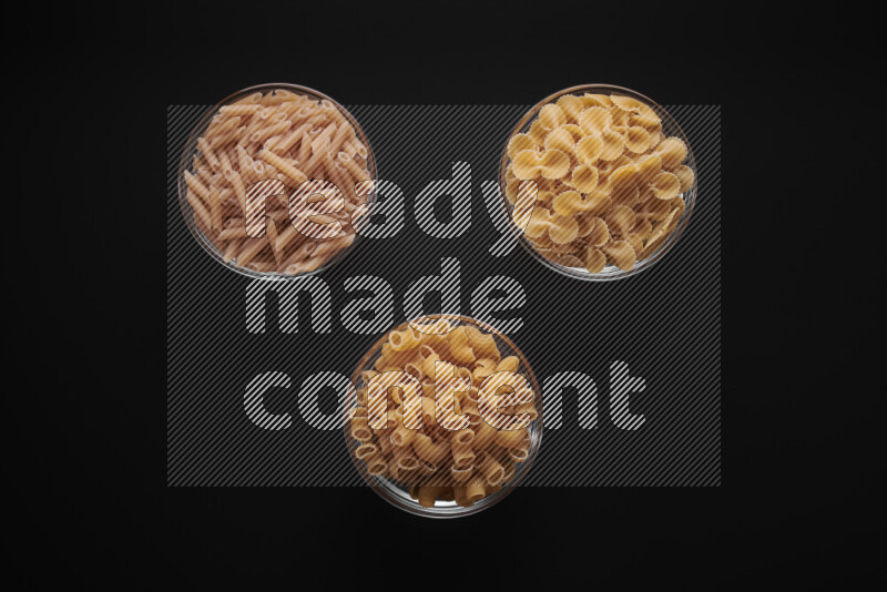 Different pasta types in glass bowls on black background