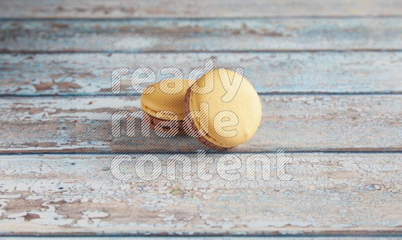 45º Shot of two Yellow and Brown Chai Latte macarons on light blue wooden background