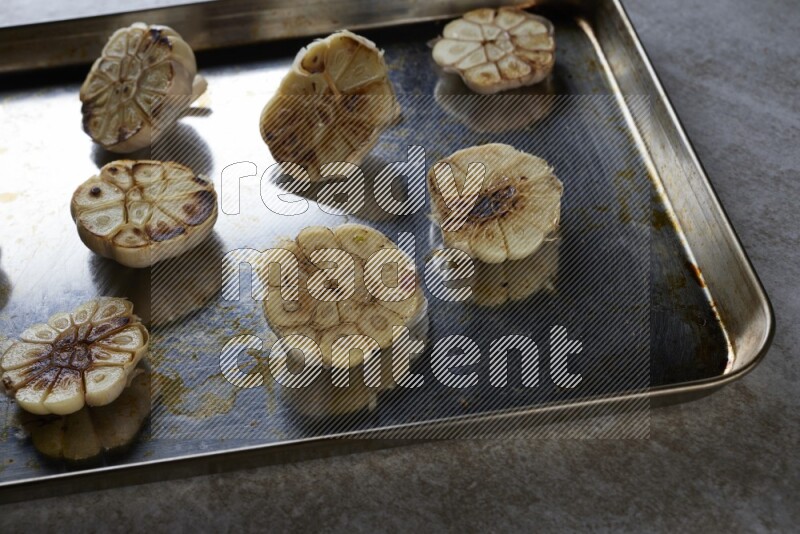 half's roasted garlic in a stainless tray on a grey textured countertop