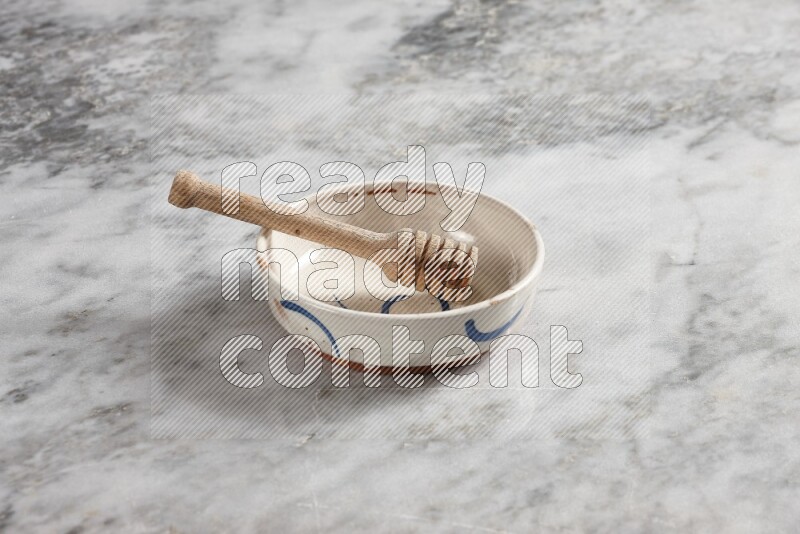 Multicolored pottery bowl with wooden honey dipper in it on grey marble background