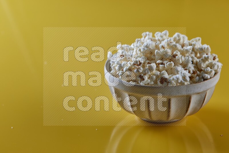 A white pottery bowl full of popcorn on a yellow background in different angles