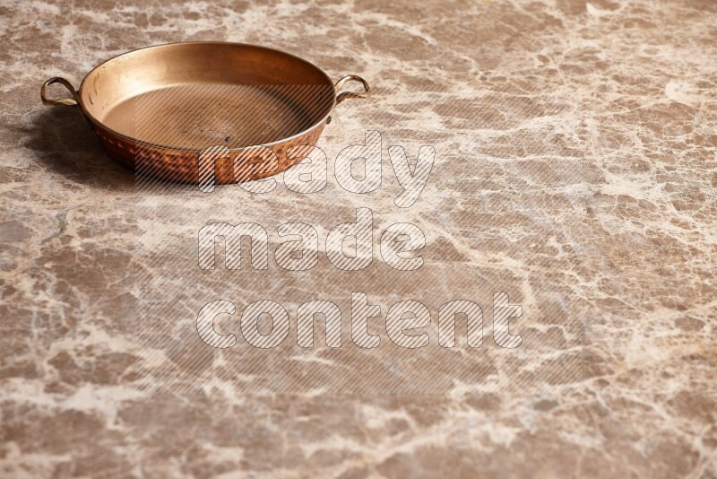 A small copper pan on beige marble background