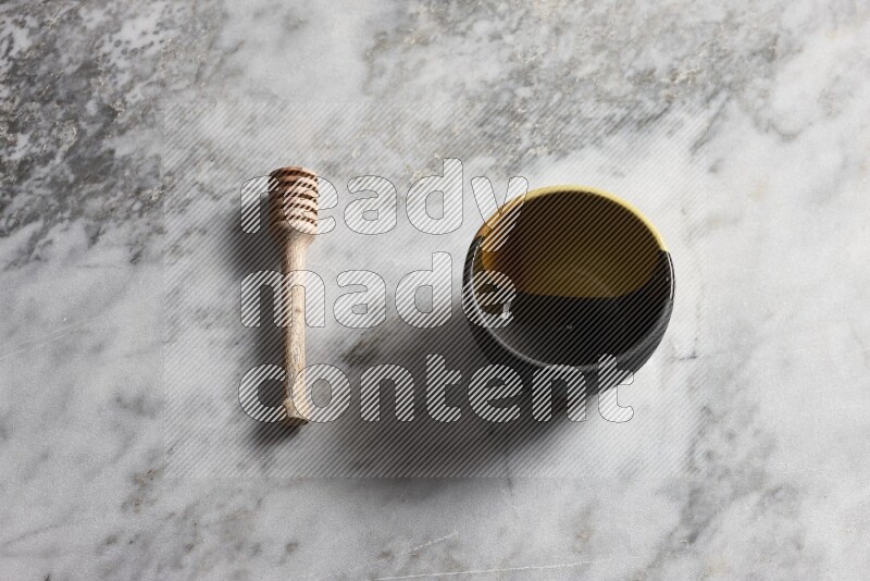 Multicolored pottery bowl with wooden honey dipper on the side on grey marble background