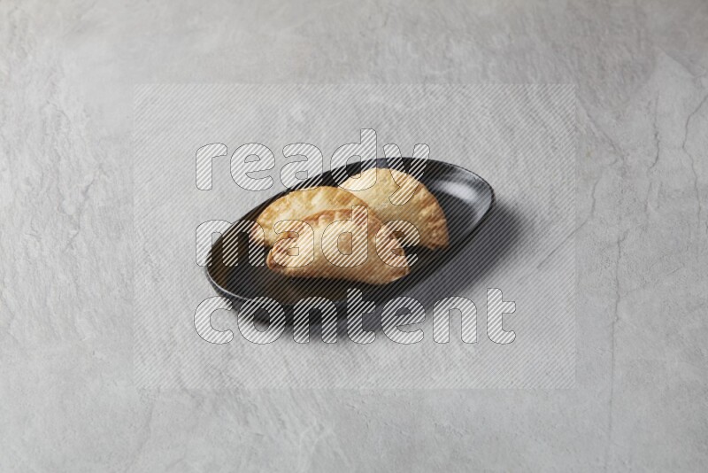 Three fried sambosas in an oval shaped black plate on a gray background