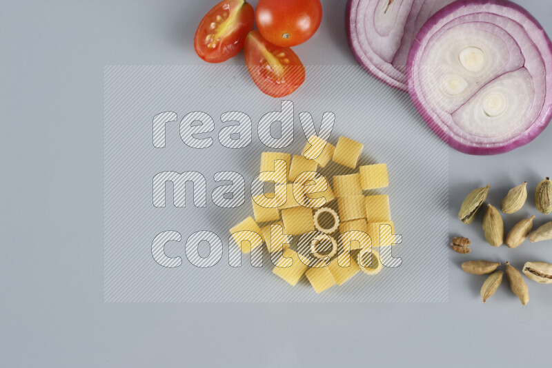 Raw pasta with different ingredients such as cherry tomatoes, garlic, onions, red chilis, black pepper, white pepper, bay laurel leaves, rosemary, cardamom and mushrooms on light blue background