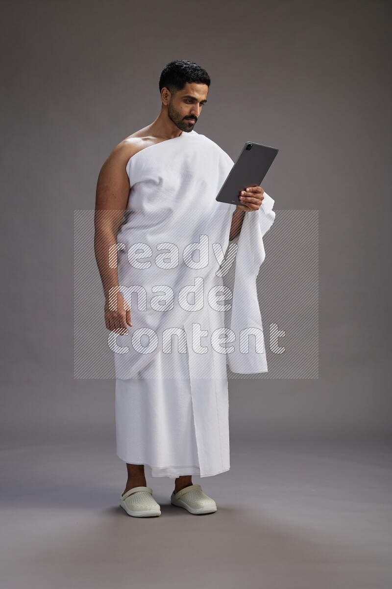 A man wearing Ehram and holding a tablet on gray background