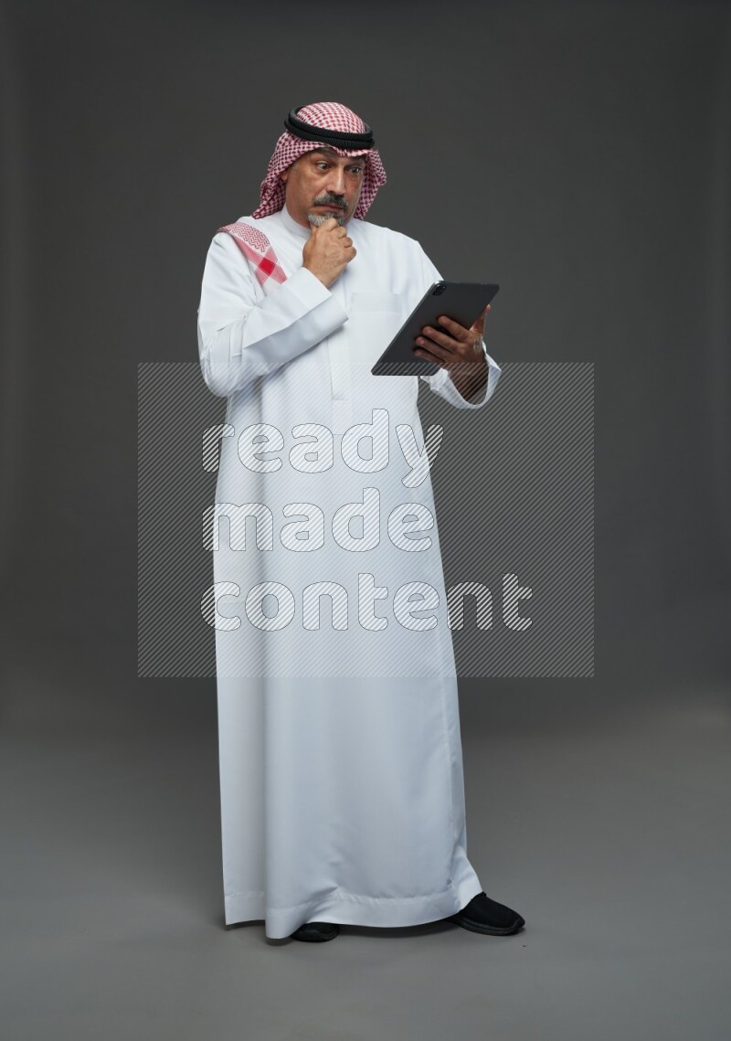 Saudi man with shomag Standing working on tablet on gray background