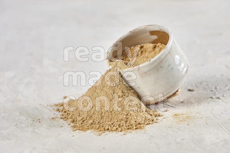 A beige pottery bowl full of ground ginger powder with fallen powder from it on white background