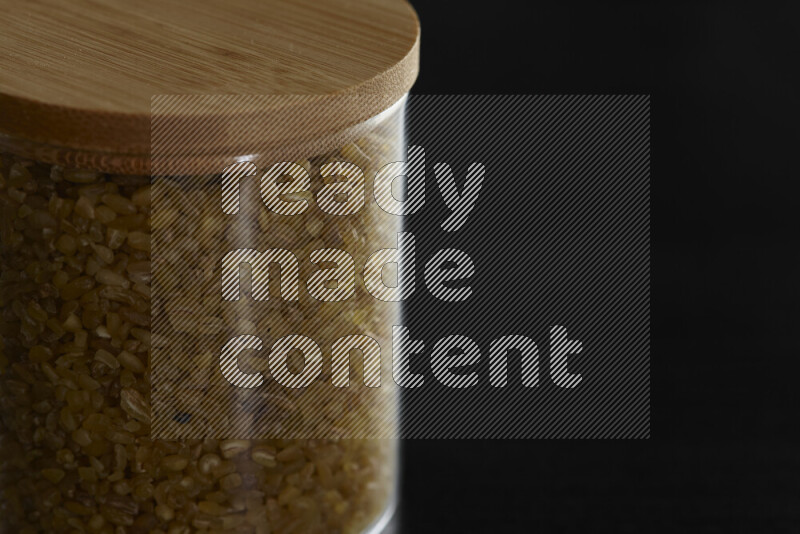 Coarse bulgur in a glass jar on black background