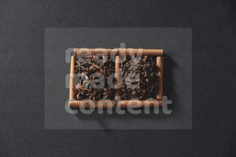 مربعان من أعواد القرفة ممتلئان باليانسون النجمي والقرنفل علي خلفية سوداء