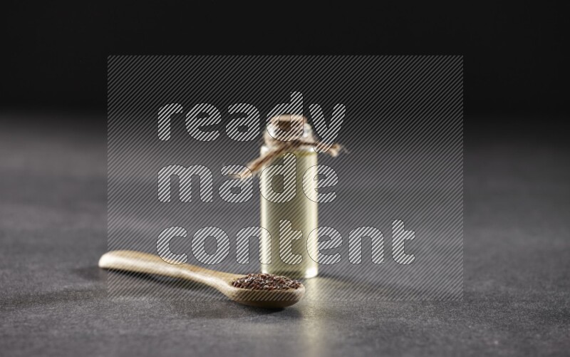 A wooden spoon full of flaxseeds with a glass bottle of flaxseeds oil on a black flooring