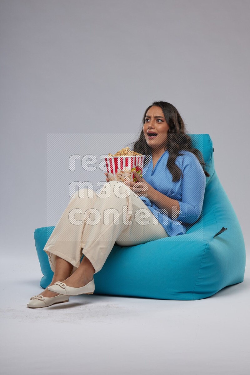 A woman sitting on a blue beanbag and eating popcorn