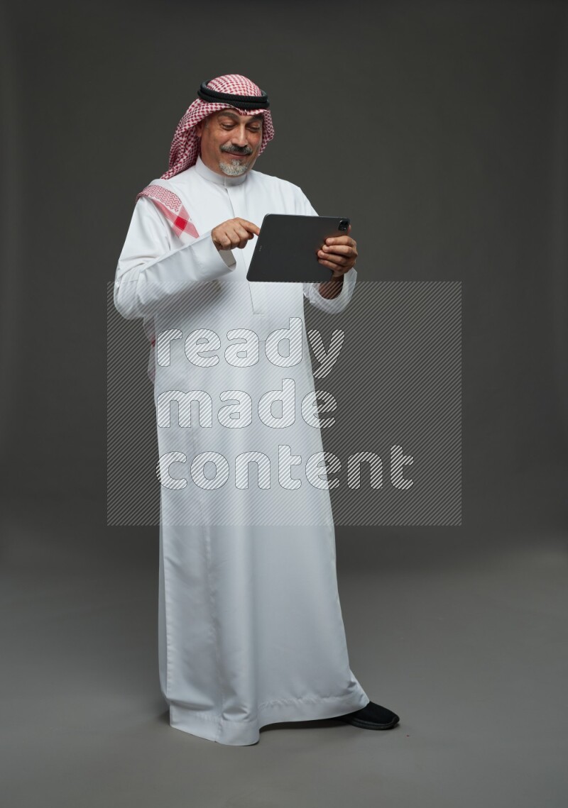 Saudi man with shomag Standing working on tablet on gray background