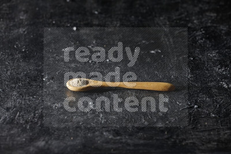 A wooden spoon full of white pepper powder on textured black flooring