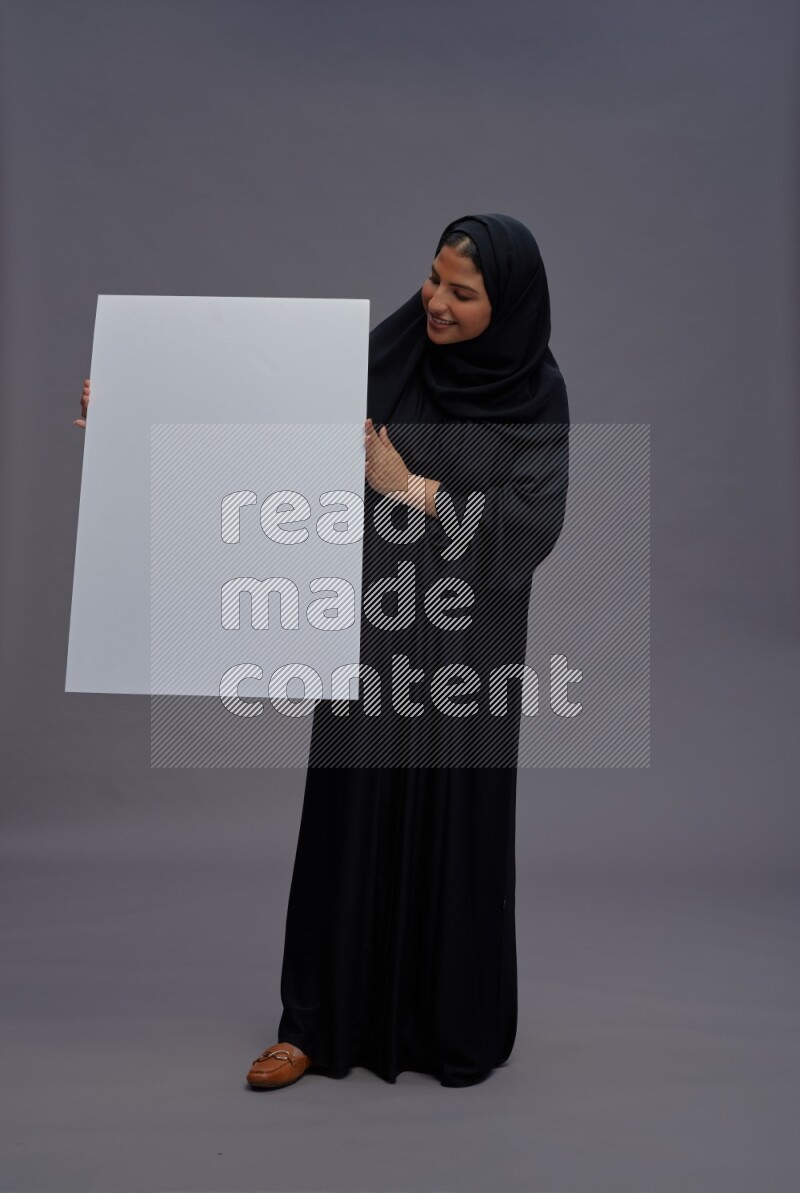 Saudi woman wearing Abaya standing holding white board on gray background