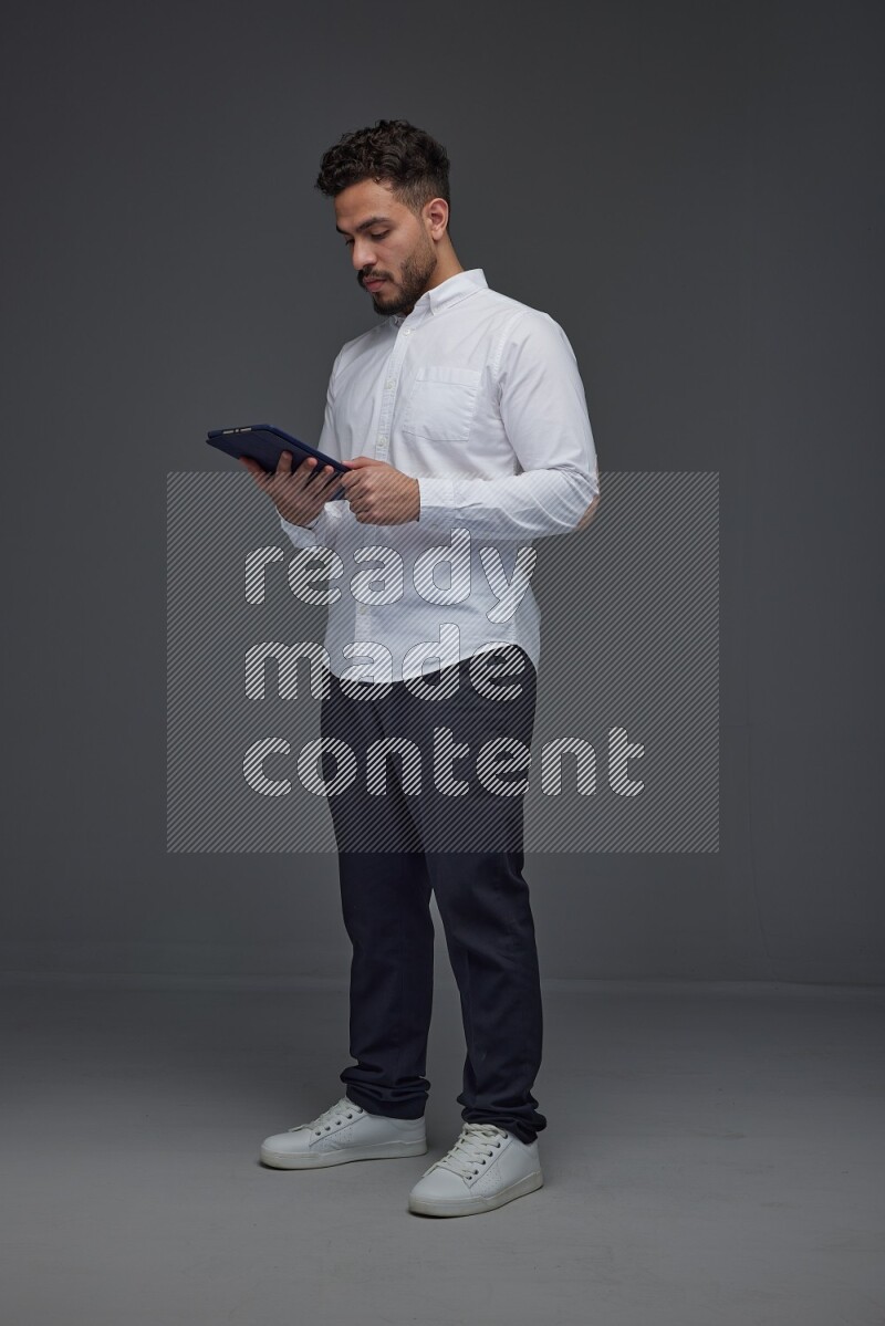 A man wearing smart casual standing and using his tablet eye level on a gray background