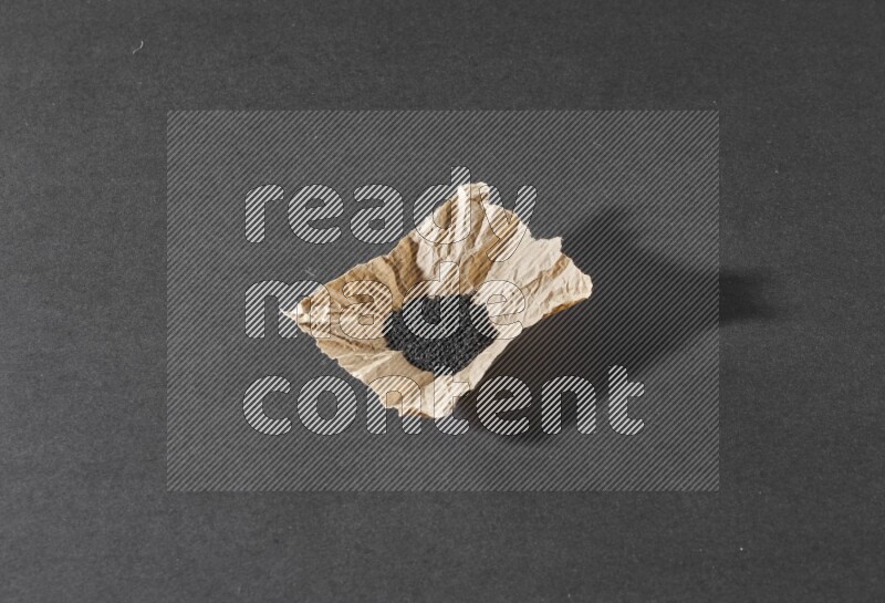 A crumpled piece of paper full of black seeds on a black flooring
