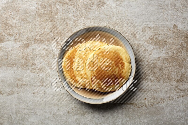 Three stacked plain pancakes in a bicolor plate on beige background