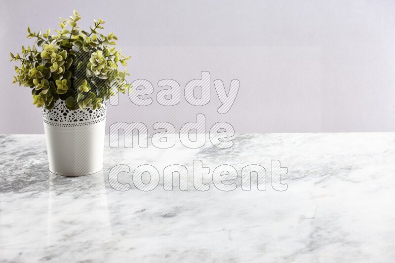 Green artificial plant in white decorative pot on grey marble background